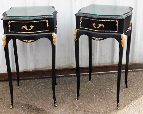 A pair of French style black and gold painted bedside cabinets, each with glass inset top, and silver drawer picked out in silver and gold, on splayed feet, 72cm high, 36cm wide, 40cm deep.