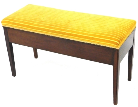 An Edwardian mahogany framed duet stool, the overstuffed hinged top revealing a plain interior, in yellow striped material, on square tapering legs, 54cm high, 80cm wide, 38cm deep.