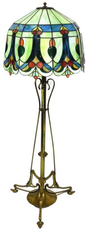 An Art Nouveau brass metamorphic lamp standard, the cylindrical stem held by swan necked supports, on a circular foot terminating in compressed leaf feet, with a later Tiffany style shade decorated in colours, with metal finial, when lowered, 130cm high.