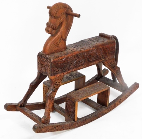 A Nepalese carved rocking horse, heavily carved floral decoration, 75cm high, 90cm long, 32cm wide.