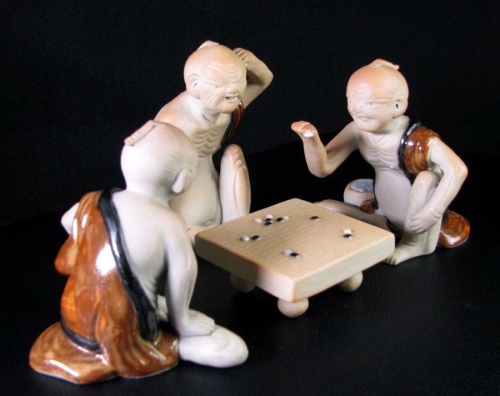 A Japanese Hirado porcelain group of men in brown robes playing the game of go', seated at a low table, 19thC, the largest figure 10cm high.