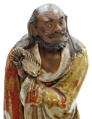 Three Chinese glazed pottery "mudmen" Immortals, each with glazed colouring, including a sage with purple robes, 34cm high, a bearded figure holding a shoe in red and green robes, 32cm high, and another sage robed in blue, hardwood bases, 13cm high. (3) - 7