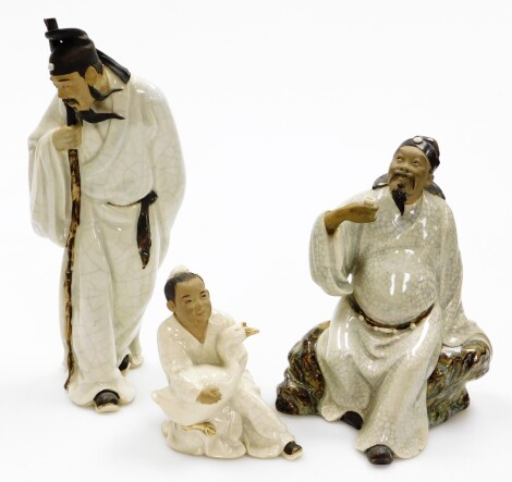 Three terrocotta and white glazed finished figures, to include a figure of a gentleman carrying staff, 29cm high, in a white glaze finish, a figure of a man seated on a rock drinking, 23cm high, and a figure of a child carrying duck, 14cm high. (3)