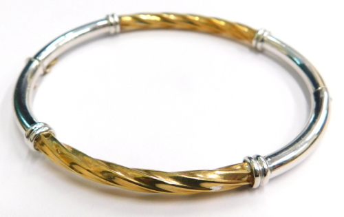 A 9ct gold hinged bangle, of two colour design, with silvered and yellow gold finish, the central panel of twist design, on hinge with safety clasp, maker's stamp H M Limited, 7cm diameter, 7g all in, boxed.