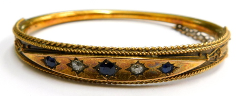 A Victorian 15ct gold hinged bangle, with a diamond shaped top section set, with sapphires and diamonds, with reeded filigree type decoration, with safety chain on hinged support 6cm diameter, 11.7g all in.