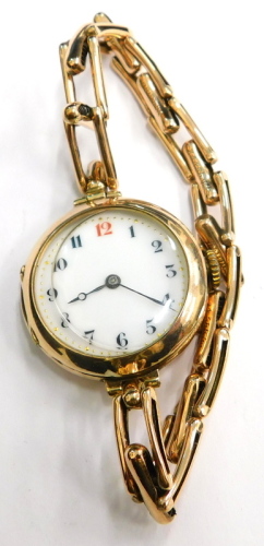 An early 20thC 9ct gold wrist watch, with circular watch head and white enamel dial, with gold markers and blue hands, on a expanding yellow metal bracelet, unmarked, 21g all in.