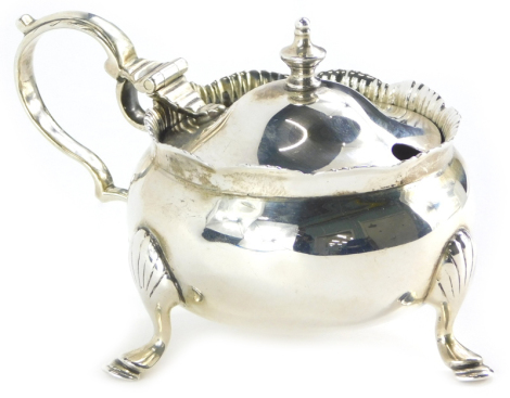 A George V circular silver mustard pot, with scroll cast handle on three feet, with blue glass liner, Chester 1911, 2¾oz.