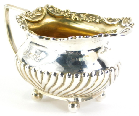 An Edwardian silver small milk or cream jug, with gilt interior, the border cast with flowers, scrolls, etc., and with a part fluted body and angular handle and bun feet, London 1900, 2¼oz.