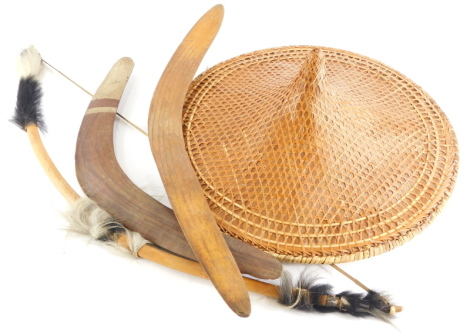 Tribal Art. An Australian Aboriginal boomerang painted in cream, 51cm wide, another boomerang, a bow and arrow, and a coolie hat.