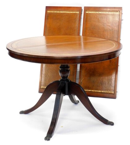 A mahogany extending dining table, the circular top with a brown tool leather insert, on turned column and reeded splayed legs, two loose leaves, 75cm high, 107cm diameter closed, 200cm extended.