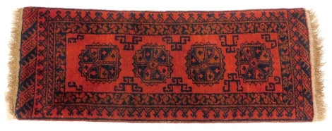 An Afghan narrow rug or runner, with a design of four medallions on an orange ground, with multiple borders, 135cm x 50cm.