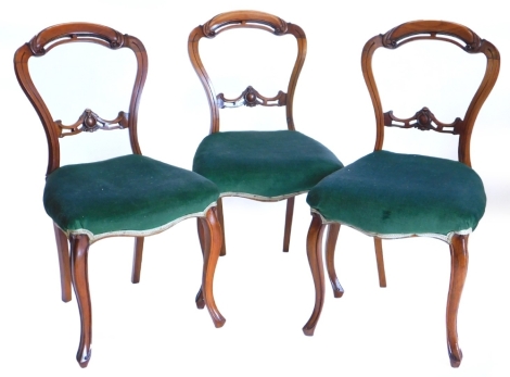 A set of three Victorian walnut balloon back chairs, each with a green padded seat, on cabriole legs.