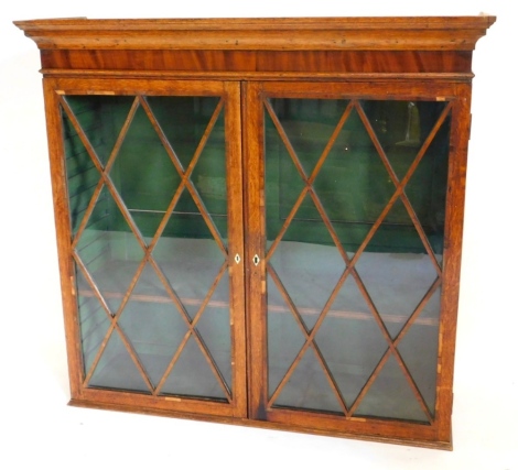 An early 19thC oak and mahogany crossbanded bookcase, with a moulded cornice above two astragal glazed doors, enclosing a single shelf, 100cm high, 105cm wide. Note: VAT is payable on the hammer price of this lot at 20%.