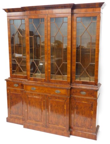 A yew veneered breakfront bookcase, in George III style with a moulded cornice, with four glazed doors, the base with a central drawer, flanked by two smaller drawers, above four panelled doors on plinth, 212cm high, 170cm wide.