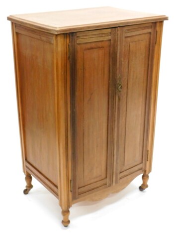 An unusual walnut side cabinet, the top with a moulded edge with two panelled doors enclosing five drawers, each with a recess brass handle, above a shaped apron on turned legs with castors, 101cm high, 63cm wide.