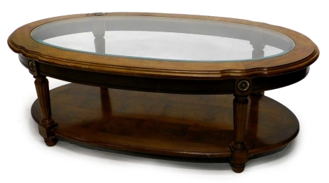 A continental walnut oval coffee table, with a bevel glass insert and an under tier, on turned and reeded legs, 115cm wide.