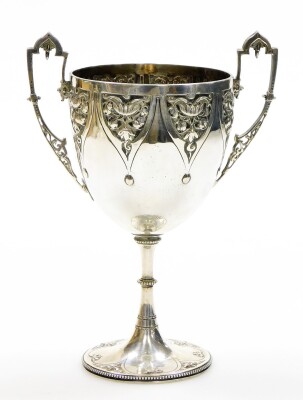 A Victorian silver two handled cup, with gothic stylised and pierced handles, and repousse floral pendant drop panels to the cup, on a chased trumpet base, engraved Thomas' 153 New Bond St., `maker WE, London 1869, with duty mark, 7½oz, 19cm high.