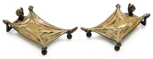 A pair of early 20thC cast bronze desk stands, being card trays formed with an outstretched figure of the Devil in bed, a humoured invitation for those to leave their cards should they wish to do business with the Devil? One cast with the maker's mark of