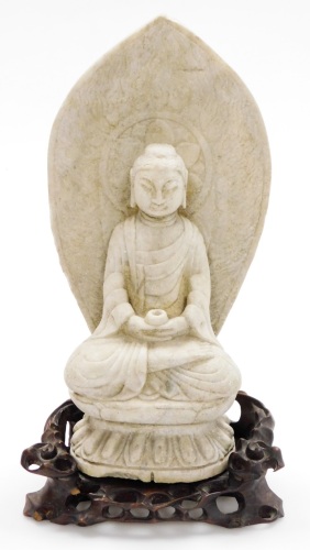 An 18thC Chinese carved stone figure of a man sat in the Lotus position holding a cup, on a carved open work wood base, 44cm high, 24cm wide, 16cm deep.