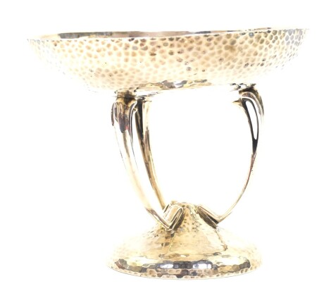 An Edward VII Art Nouveau silver circular sweet meat dish on stand, with a hammered finish, raised on three sinuous scroll supports, over a conical base, Goldsmiths & Silversmiths Company Ltd, London 1905., 10.02oz.