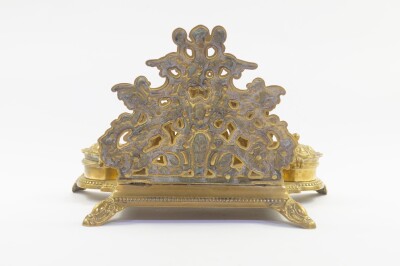 A Victorian rococo style brass desk stand, cast with cherubs, winged beasts and vase of flowers, having a letter rack pen tray and double ink wells, 30cm wide. - 2