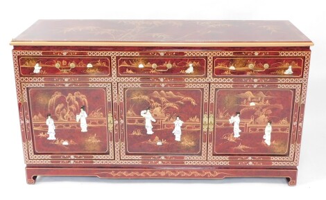 A Chinese red lacquer and 'Shibyama' sideboard, the top painted with bamboo, over three drawers above cupboard doors, raised on a bracket plinth base, 84cm high, 150cm wide, 48cm deep.