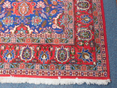 A Kashan rug, blue ground decorated with floral motifs, within a floral border against a red ground, 215cm x 330cm. - 2