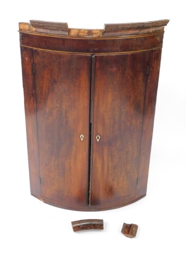 A Georgian mahogany and line inlaid bow front hanging corner cupboard, the outswept pediment over two doors, opening to reveal two shelves, 104.5cm high, 69cm wide, 50cm deep. (AF)