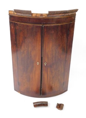 A Georgian mahogany and line inlaid bow front hanging corner cupboard, the outswept pediment over two doors, opening to reveal two shelves, 104.5cm high, 69cm wide, 50cm deep. (AF)