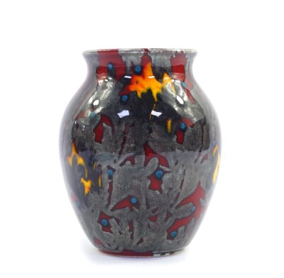 A Poole Pottery flame vase, decorated in silver with a sea weed pattern, against a red ground, raised marks, 17cm high.