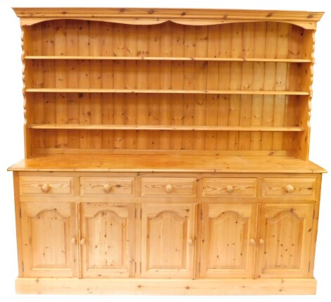 A pine dresser, the outswept pediment over a three shelf plate rack, above five short drawers, over channeled cupboard doors, raised on a plinth base, 198cm high, 213cm wide, 45cm deep.