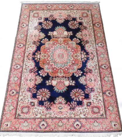 A Pakistan dark blue ground rug, decorated in red, pink and blue with palmettes and floral motifs around a central medallion, 276cm x 185cm.