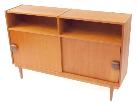 A mid century teak sideboard, possibly Danish, with two recesses above a pair of sliding doors, enclosing two shelves, raised on tapering square legs, 79cm high, 122cm wide, 29cm deep.