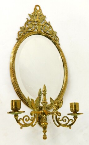 A Victorian brass girandole, the oval framed mirror inset bevelled glass, with a surmount cast with a bird on a plinth and arabesques, the two branch candle holder with bird of paradise, scrolling arms, 52cm high, 21cm wide.