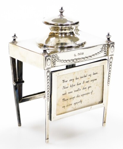 An early George V silver ink stand of neo classical design, having a raised inkwell on a four leg stand, with urns, oval patera and bell husk pendants, the legs tied by revolving card cases to the front and rear of the frame, maker John Round & Son, Sheff