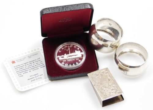 A group of silver wares, to include a silver book cover, (AF), two silver napkin rings, one bearing the initial F, Birmingham and another of plain design Sheffield assay, 1¼oz, together with a Canadian dollar mint silver collectors coin, cased. (4)