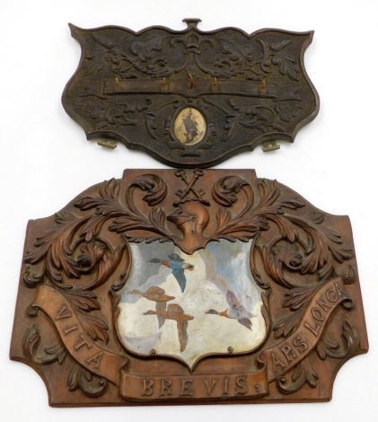 Two carved oak wall plaques, to include one with painted central shield of flying ducks and bearing the emblem Vita Brevis Ars Lonca, 45cm x 33cm, together with a later coat hook, 26cm x 37cm. (2)