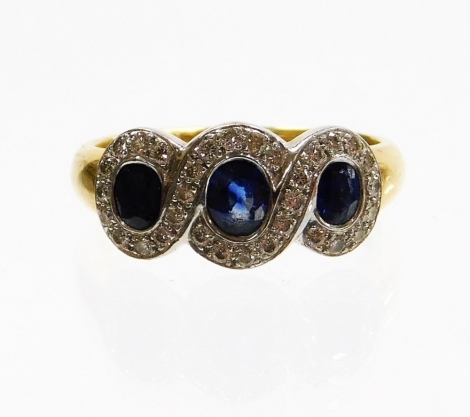 An 18ct gold sapphire and diamond dress ring, the three design section each with oval cut sapphire in rub over setting surrounded by a twist design white gold surround, set with tiny diamonds on a yellow gold band, ring size Q, 5.7g all in, boxed.