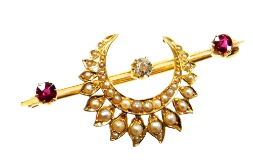 An Eastern inspired bar brooch, set with diamond, ruby and applied crescent moon and flower set seed pearl surround, the old cut diamond in six claw setting, 3.2mm x 2.4mm, approx 0.10cts, flanked by two old cut rubies in a similar setting, 3.8mm x 2.4mm,