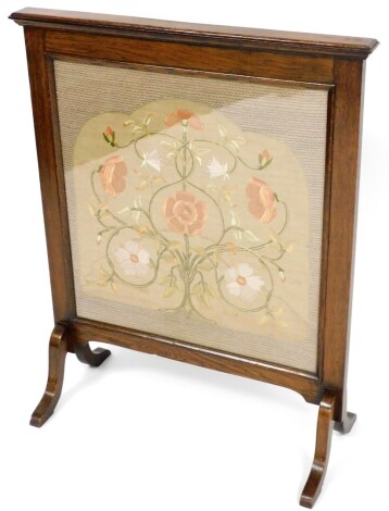 A Victorian needlework fire screen, in a later oak surround, the central panel in silver depicting pink and cream flowers on splayed legs, 90cm high, 71cm wide, approximately 23cm deep.