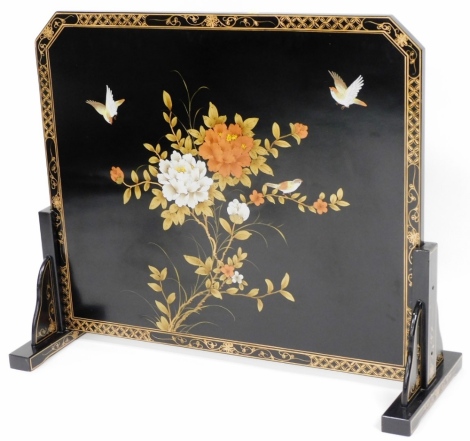 A black Japanned lacquer fire screen, with a gilt border decoration of flowers leaves and bird on two stand base, with gold leaf back, with a shaped top, 81cm high, 87cm wide, 26cm deep.