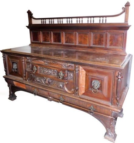 A Victorian mahogany Gothic style sideboard, the upper section with a scroll top held by shaped spindles, flanked by moulded columns, above plain panels, the subsection with three heavily carved drawers set with lions mask and metal handles, scroll and fa