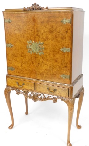 A figured walnut cocktail cabinet, with scroll Fleur De Lis panelled top on two doors each with metal attachments on splay legs, 157cm high, 84cm wide, 43cm deep.