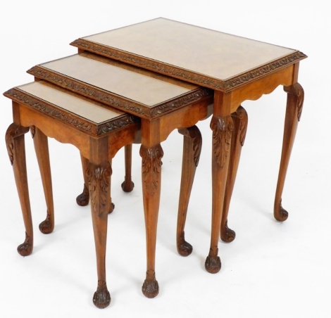 A set of walnut carved nest of three tables, each with glass inset top, on a carved border with carved feet, the largest 56cm high, 56cm wide, 40cm deep.