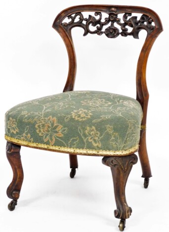 A Victorian carved mahogany nursing chair, the wooden back with fleur de lys and floral carving, on a green rough material seat, with shell legs and castors, 69cm high, 47cm wide, 44cm deep.