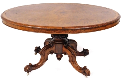 A fine Victorian burr walnut and marquetry breakfast table, with cross banded oval quarter veneered tilt top, and a jewel carved central pillar on heavy moulded cabriole legs with brass and ceramic castors, 74cm high, 146cm wide, 113cm deep.