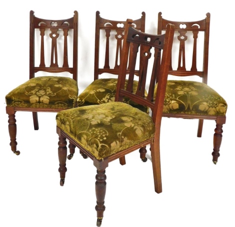 A set of four late Victorian Arts & Crafts mahogany stained dining chairs, each with shaped pierced back splats, overstuffed seats in green floral material, on turned front legs, terminating in castors, 103cm high. (4)