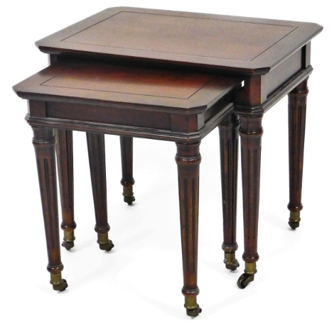 A nest of two 20thC mahogany finish tables, each canted on cylindrical turned reeded graduated legs terminating in castors, the largest 50cm high, 54cm wide, 40cm deep.