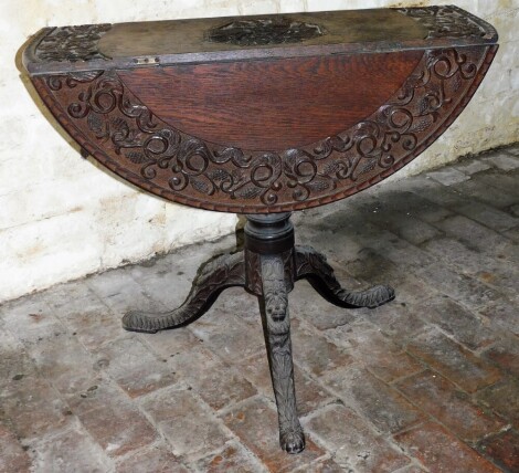 An Georgian carved oak drop leaf supper table, with a central carved decoration of lilies and vines, on lion mask carved tripod base with two drop leaves, 72cm high, 90cm wide, 88cm diameter.