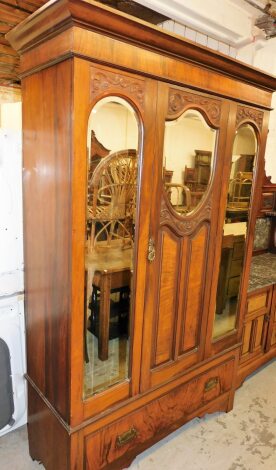 An Edwardian walnut triple wardrobe, with moulded cornice above three panelled section with single door and two outer panels set with mirror on a drawer base with brass handles, 203cm high, 122 wide, 46cm deep.